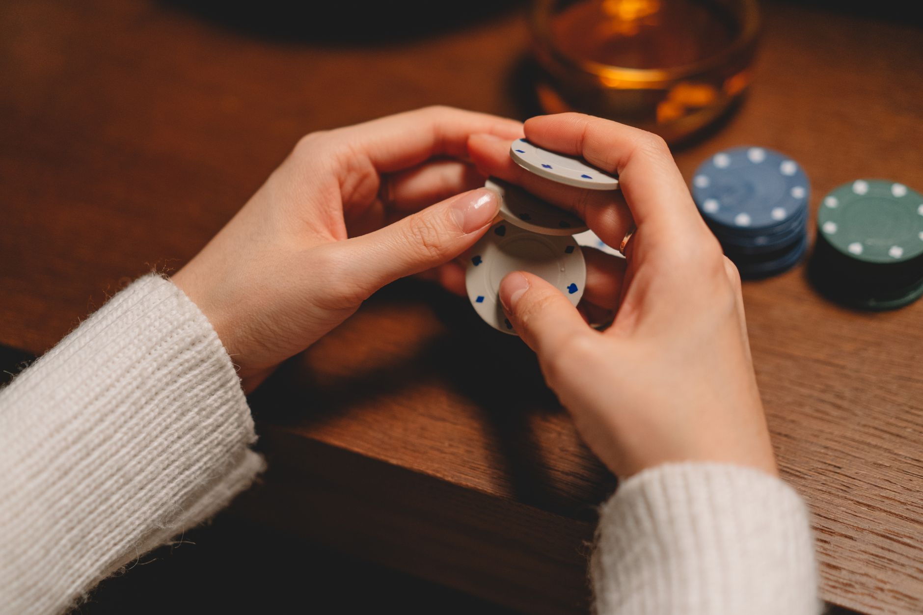 A person in a white sweater playing with poker chips on a wooden table. — What should you really understand to earn the most